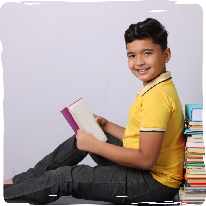 A young intelligent boy is sitting behind a pile of books and reading a book